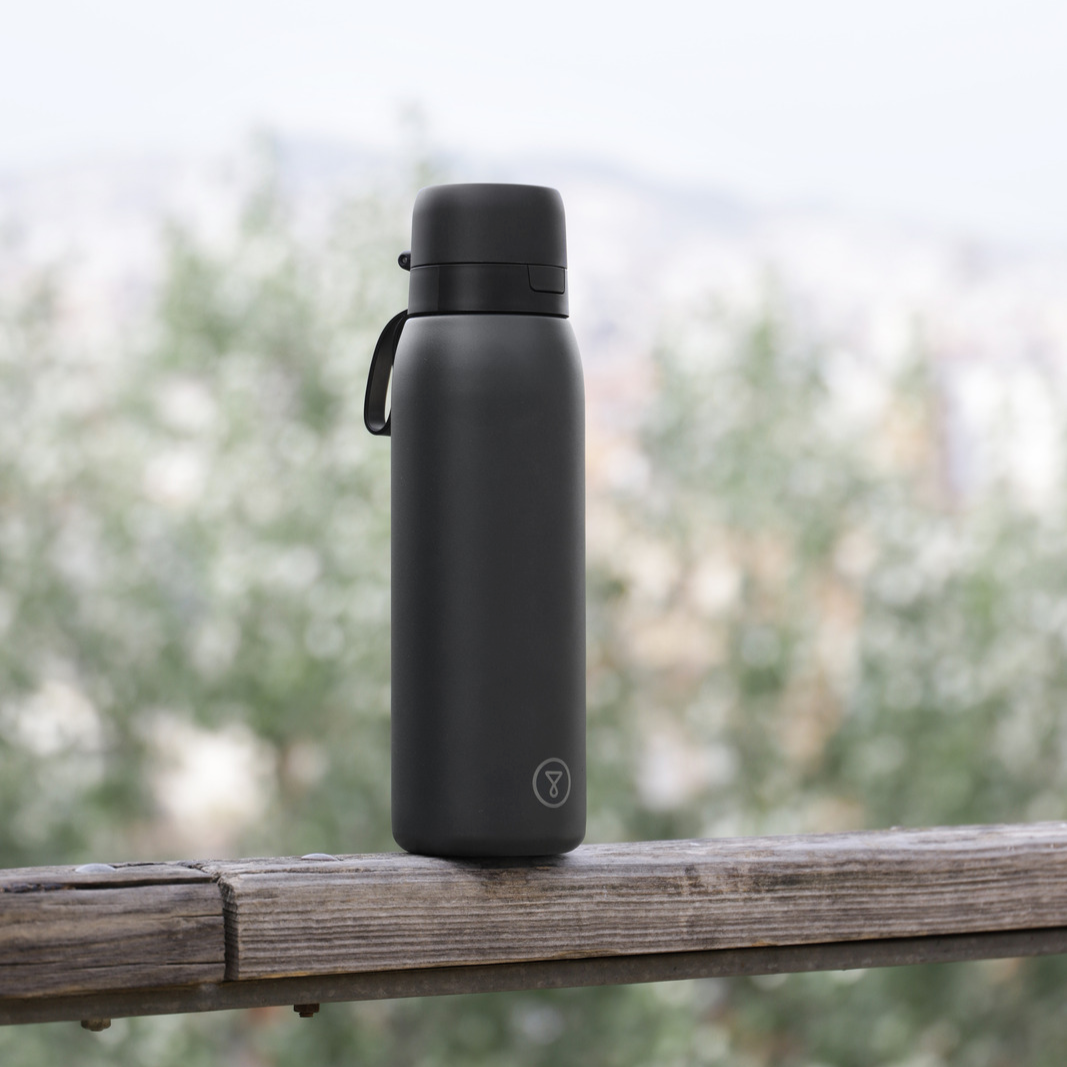 A black stainless steel water bottle with a flip-top lid on a light blue background.