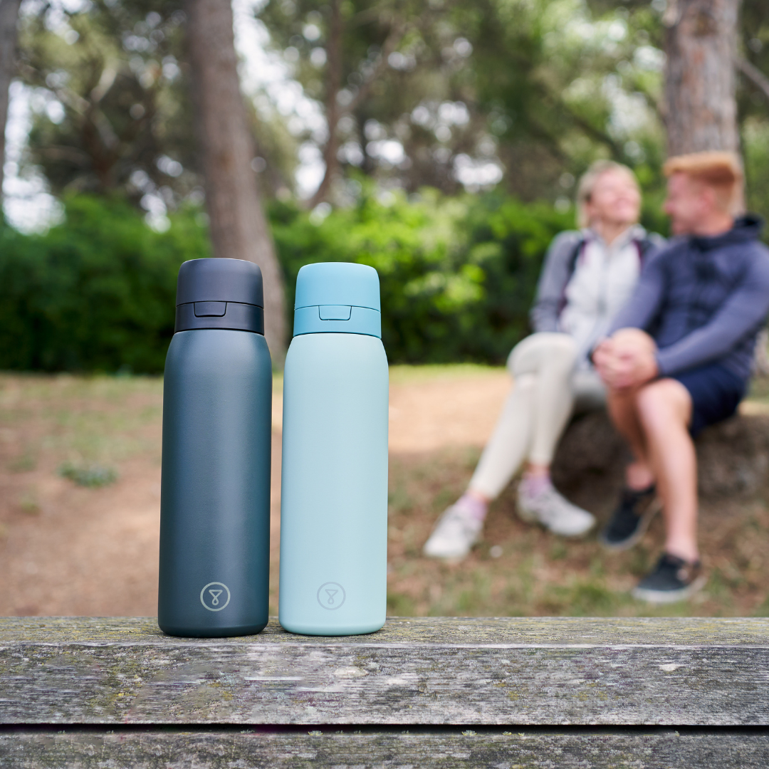 A black stainless steel water bottle with a flip-top lid on a light blue background.