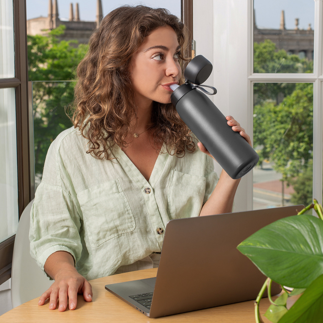 A black stainless steel water bottle with a flip-top lid on a light blue background.